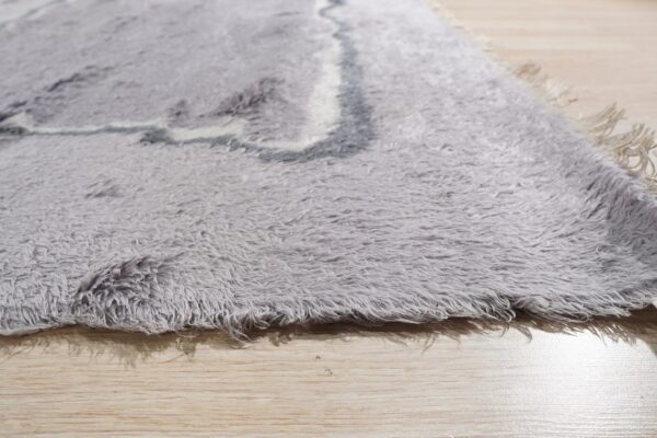 Detail view of a gray shaggy rug showing long pile, abstract curves, and light wood planks.
