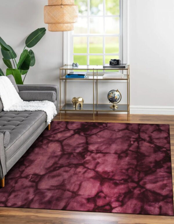 Abstract burgundy and dark purple rug grounding a gray sofa and brass console table on wood flooring.