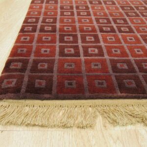Geometric rust and maroon rug with gray grid pattern and tan fringe on light wood floor.
