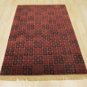 Red and dark maroon rug with nested square geometric pattern and fringe on blonde wood floor.