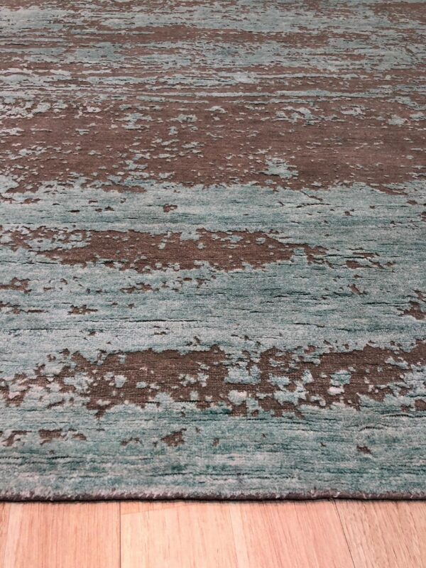 Abstract teal and brown rug featuring horizontal distressed stripes sits angled on light wood planks.
