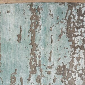 Textured rug in aqua and taupe features an abstract distressed pattern lying on light wood flooring.