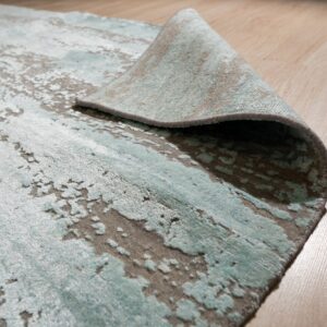 Abstract aqua and gray high-low pile rug is folded back, resting on a light wood floor.