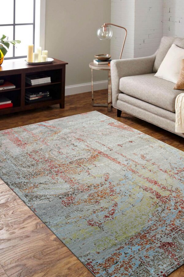 Faded gray low-pile rug with colorful distressed red and blue abstract patterns anchors a neutral living room.