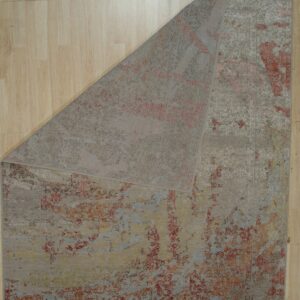 Low-pile taupe rug with distressed red and gold pattern, folded back on light wood flooring.