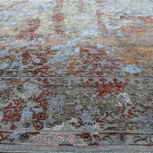 Angled view of a low-pile gray area rug with colorful abstract floral details on light wood flooring.