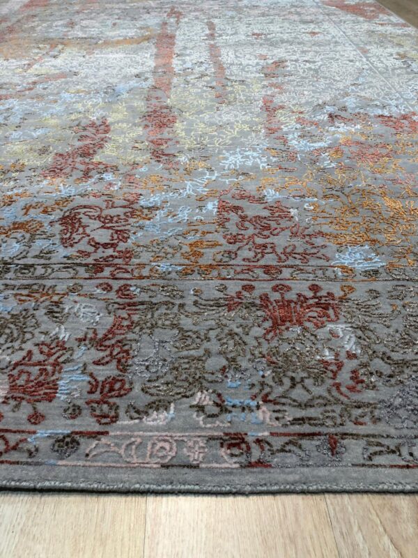 Angled view of a low-pile gray area rug with colorful abstract floral details on light wood flooring.