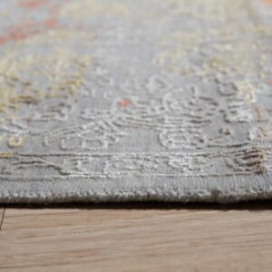 Low-angle detail of a short-pile gray rug featuring carved beige and rust ornamental patterns on wood flooring.