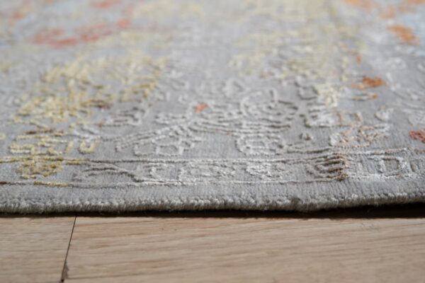 Low-angle detail of a short-pile gray rug featuring carved beige and rust ornamental patterns on wood flooring.