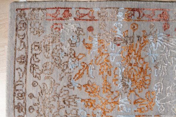 High-pile gray rug with traditional orange, blue, and brown patterns rests on light wood flooring.