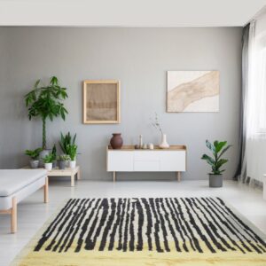 Shaggy black and cream striped rug with a yellow end sits on light flooring in a minimalist gray room.