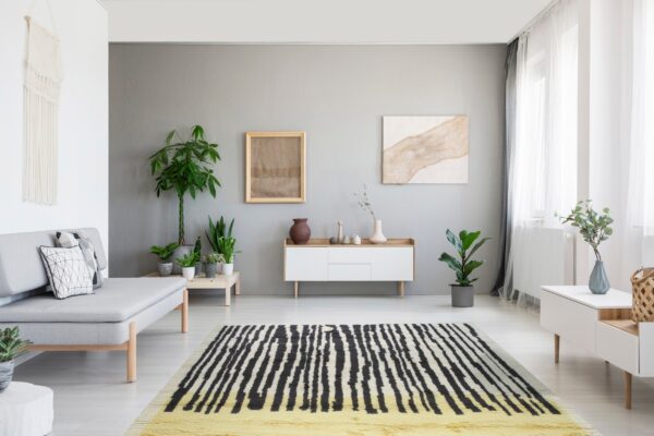 Shaggy black and cream striped rug with a yellow end sits on light flooring in a minimalist gray room.