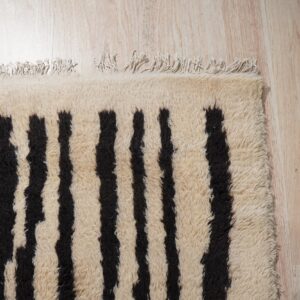 High-pile cream rug featuring bold, irregular black vertical stripes and tassels on light wood flooring.