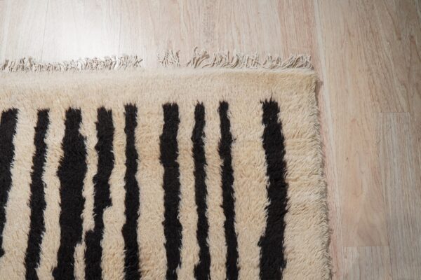 High-pile cream rug featuring bold, irregular black vertical stripes and tassels on light wood flooring.