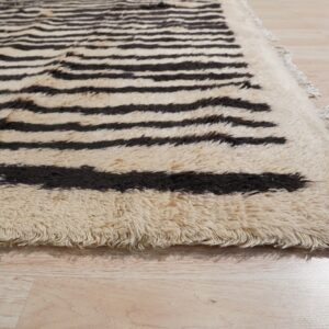 Shaggy cream rug with dark brown horizontal stripes and fringe resting on pale wood floorboards.