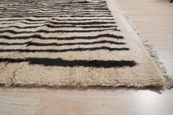 Shaggy cream rug with dark brown horizontal stripes and fringe resting on pale wood floorboards.