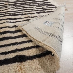 Shaggy cream and dark brown horizontally striped rug folded to reveal the backing on light wood flooring.