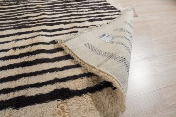 Shaggy cream and dark brown horizontally striped rug folded to reveal the backing on light wood flooring.