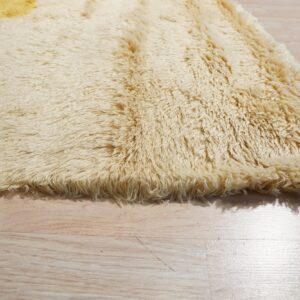 Close-up of a cream and golden yellow shaggy rug with a long pile texture on light wood flooring.