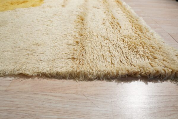 Close-up of a cream and golden yellow shaggy rug with a long pile texture on light wood flooring.