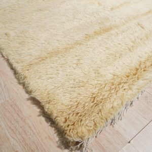Shaggy high-pile rug in off-white, yellow, and black abstract patterns rests on pale wood floor.
