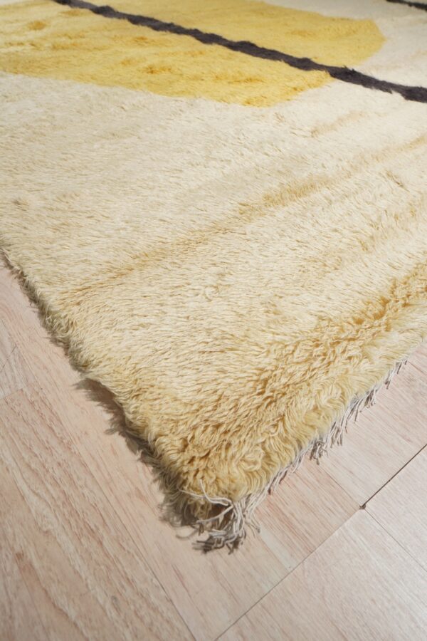 Shaggy high-pile rug in off-white, yellow, and black abstract patterns rests on pale wood floor.