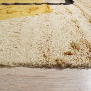 The high-pile, shaggy rug edge shows cream, mustard, and dark brown geometric patterns over light wood floor.