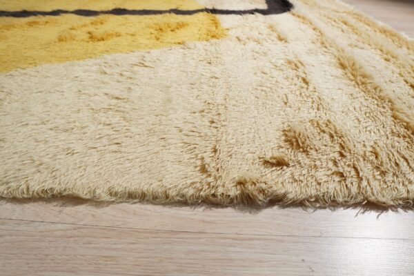 The high-pile, shaggy rug edge shows cream, mustard, and dark brown geometric patterns over light wood floor.