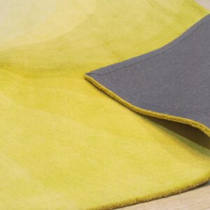 A yellow ombre rug rests on wood flooring, showing its plush pile and contrasting dark gray backing.