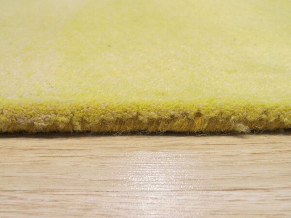 The edge of a bright yellow high-pile rug rests on a shiny, light wood floor surface.