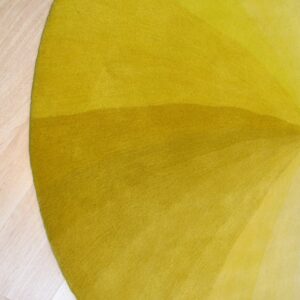 Close-up of a circular rug showing radial ombre shading from dark chartreuse to light yellow on light wood flooring.