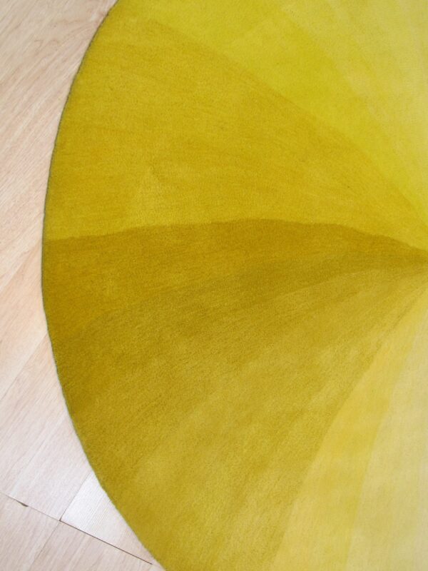 The curved edge of a medium-pile yellow rug with a subtle color gradient rests on light wood flooring.