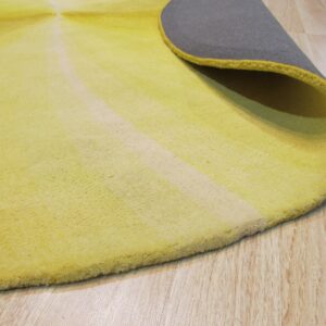 Yellow radial patterned rug curled to show the gray backing, lying on pale wood plank flooring.
