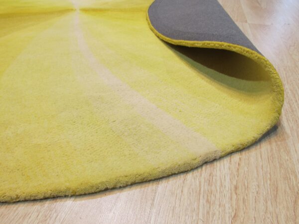 Yellow radial patterned rug curled to show the gray backing, lying on pale wood plank flooring.