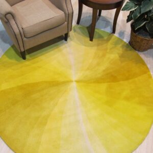 Circular yellow rug with radiating gradient stripes sits beneath a tan armchair and small wood table.