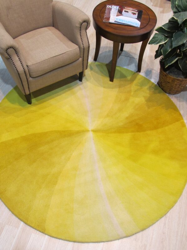 Circular yellow rug with radiating gradient stripes sits beneath a tan armchair and small wood table.