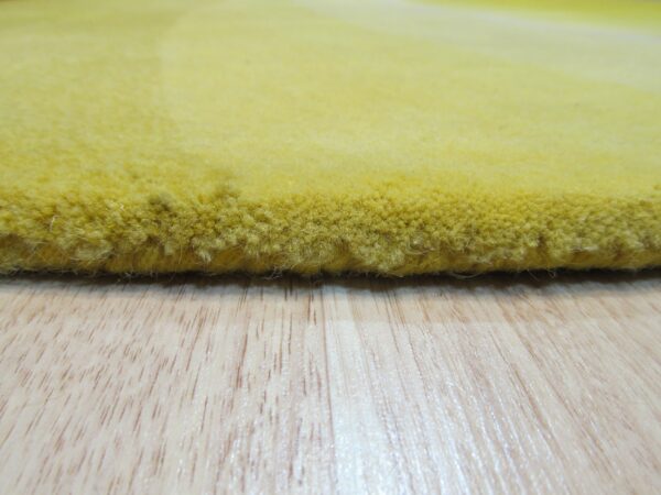 The dense, high pile edge of a yellow rug rests on light wood grain flooring.