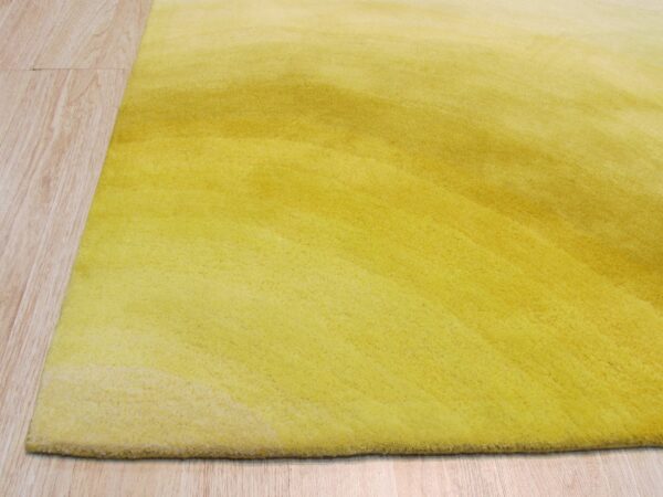 A plush yellow rug with a subtle ombre pattern rests on pale wood plank flooring.