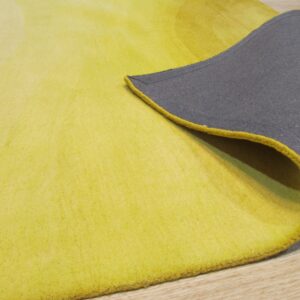 Bright yellow rug with subtle shading is peeled back, revealing a dark gray backing and light wood floor.