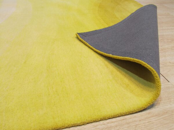 Bright yellow rug with subtle shading is peeled back, revealing a dark gray backing and light wood floor.