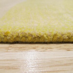 Detailed view of a thick yellow rug edge and plush pile resting on glossy light-toned wood flooring.