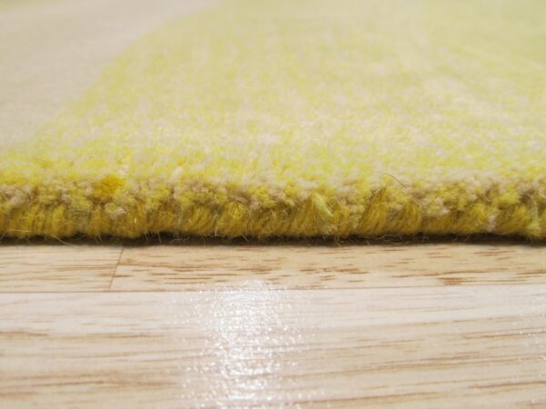 Detailed view of a thick yellow rug edge and plush pile resting on glossy light-toned wood flooring.