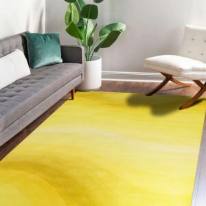 A yellow ombre rug on dark wood floors is bordered by a gray sofa and a white wood-legged chair.