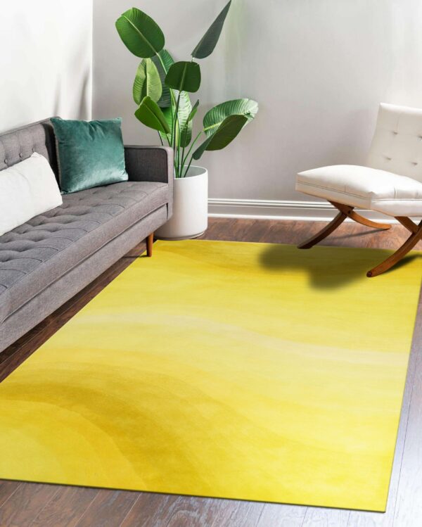 A yellow ombre rug on dark wood floors is bordered by a gray sofa and a white wood-legged chair.