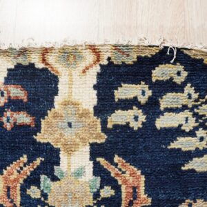 Thick pile, dark blue rug featuring beige and rust patterns with a short fringe on light blonde wood flooring.
