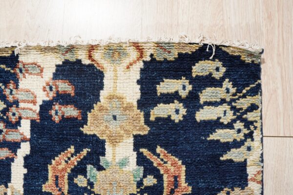 Thick pile, dark blue rug featuring beige and rust patterns with a short fringe on light blonde wood flooring.
