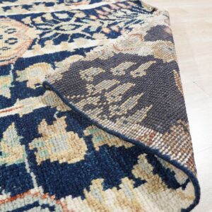 Navy blue patterned rug with ivory and beige accents folded over, showing the backing on blonde wood floors.
