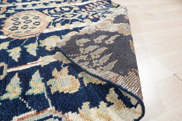 Navy blue patterned rug with ivory and beige accents folded over, showing the backing on blonde wood floors.