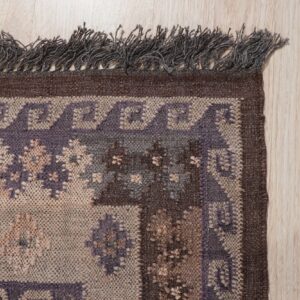 Textured rug border in brown, beige, and purple geometric patterns with dark fringe on light wood.