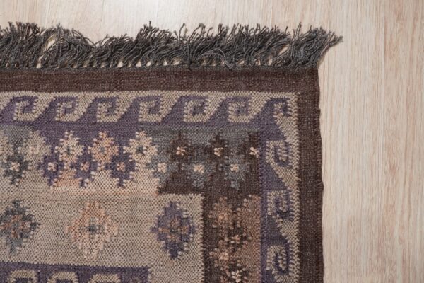 Textured rug border in brown, beige, and purple geometric patterns with dark fringe on light wood.